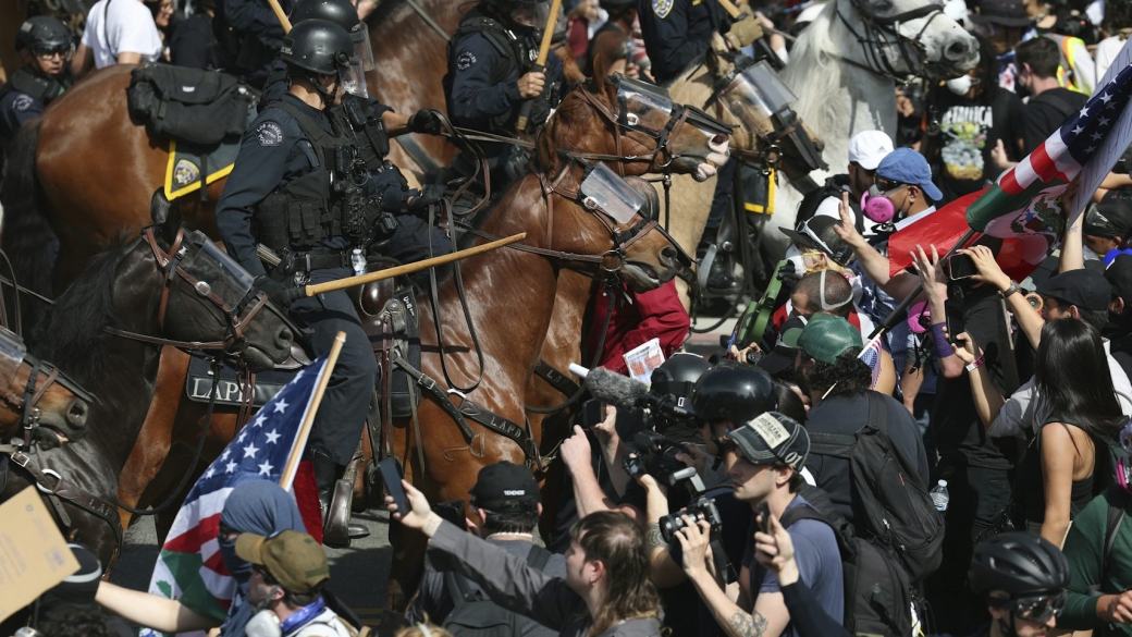 Police on horses with batons out stand amidst smartphone-wielding protesters.