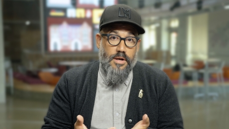 Robert Hernandez wears glasses and a hat as he speaks to the camera in the Wallis Annenberg Hall Atrium.