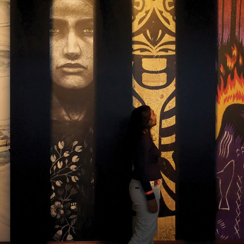 A woman walks past large murals of different art on a wall