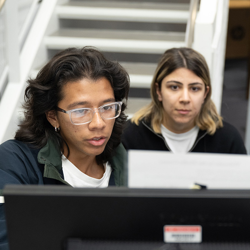 Two people work together at a computer by a staircase