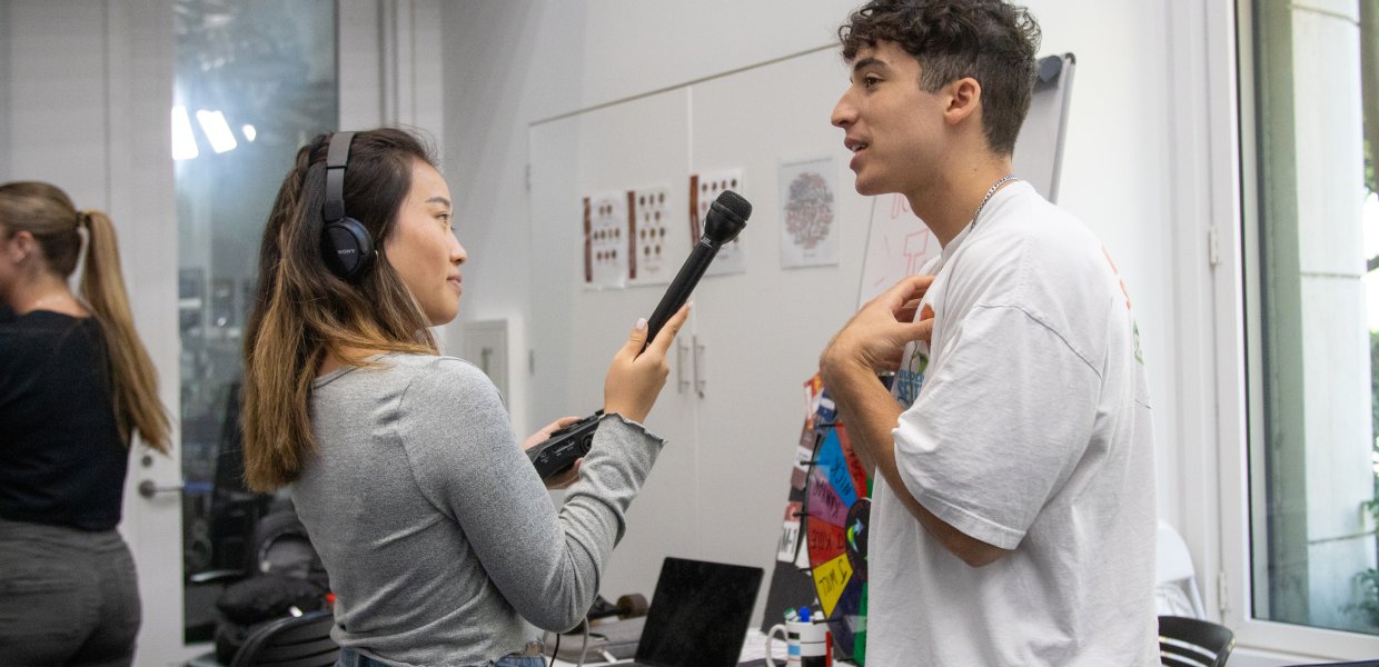 Asian female college student holds microphone and interviews male Hispanic college student