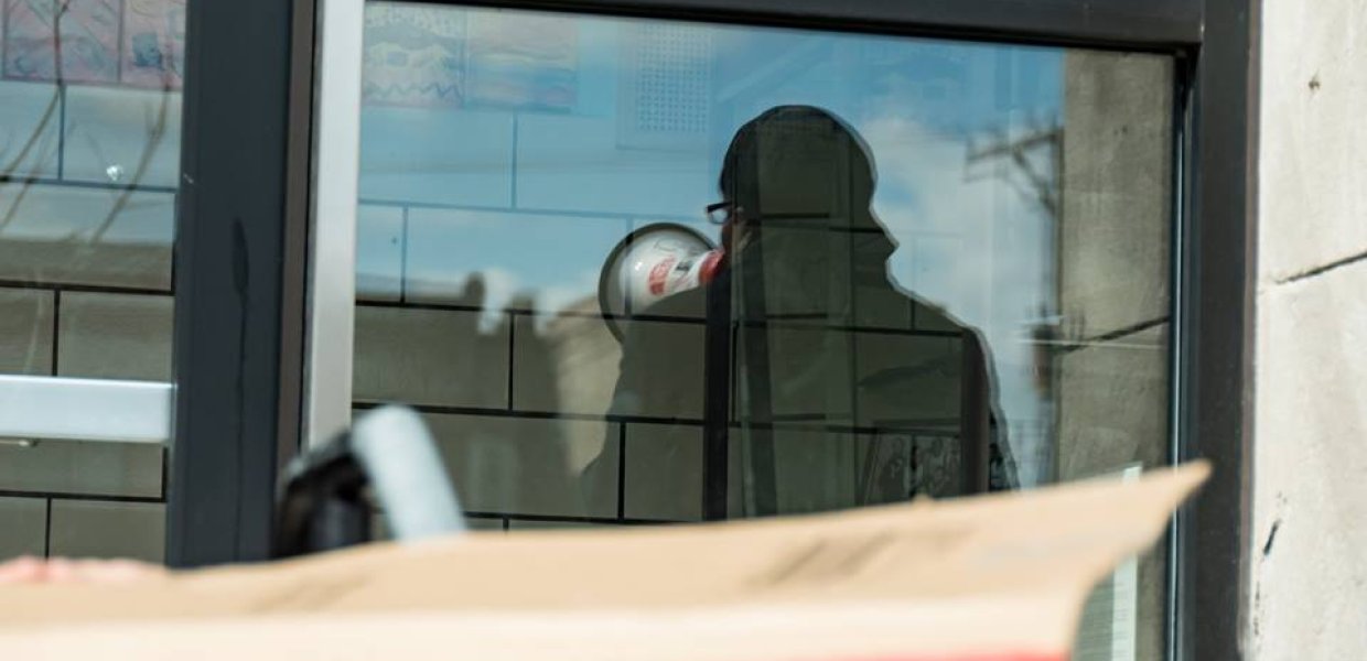 A photo of a window with a reflection of a person with a megaphone.