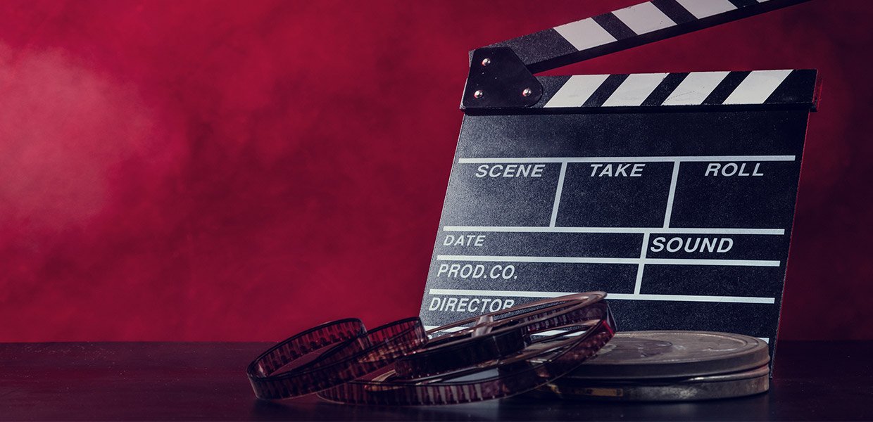 director's slate and movie film on table in front of gradient red background