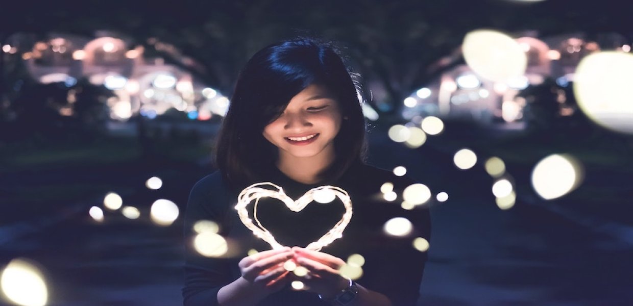 Photo of a person standing in front of many lights holding a light in the shape of a heart