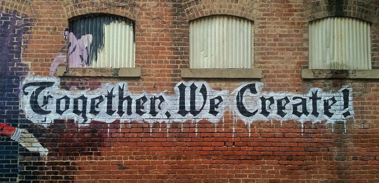 Brick wall with art that reads "Together We Create!"