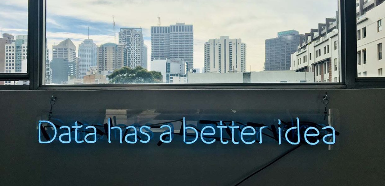 Photo of a blue neon sign under a city window that reads "data has a better idea"