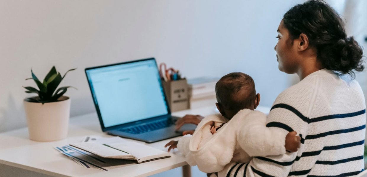 Photo of a person on a laptop holding a small child