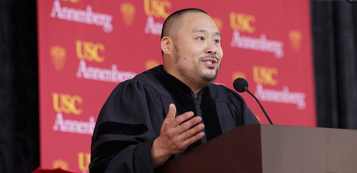 David Chang in graduation regalia address crowd in front of USC Annenberg banner