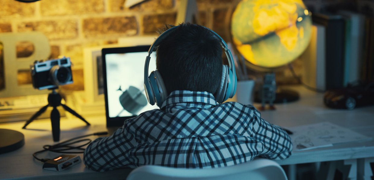 Photo of a person at a computer wearing headphones in front of a computer next to a camera