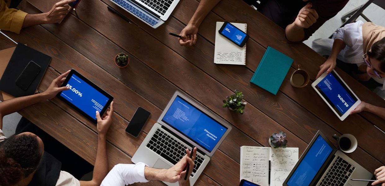 Photo of people working at a table with devices. 