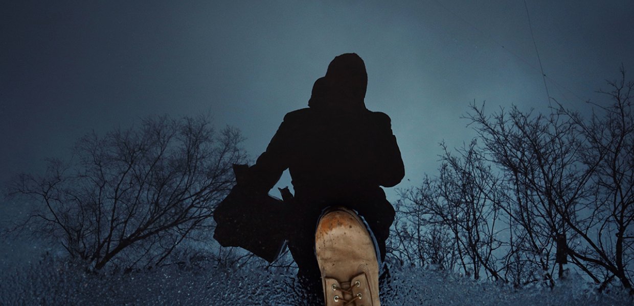 Photo of a dark silhouette with a boot next to it and a cold dead winter landscape