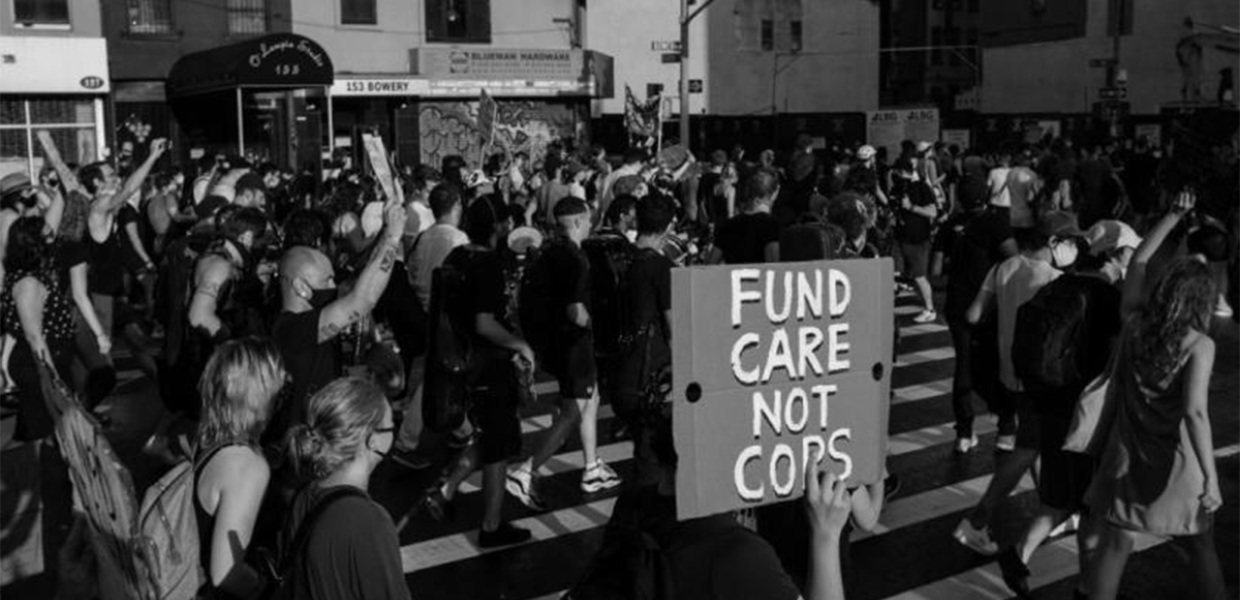 Photo of a protest with a visible sign that reads "fund care not cops"