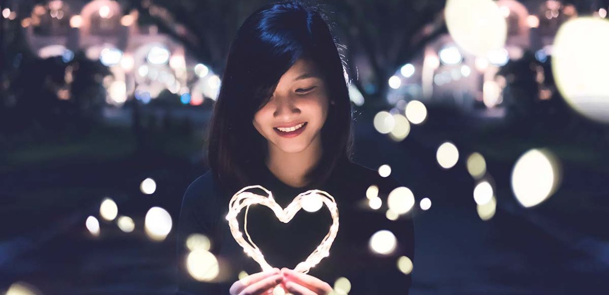 Image of a person surrounded by lights holding a heart made of light