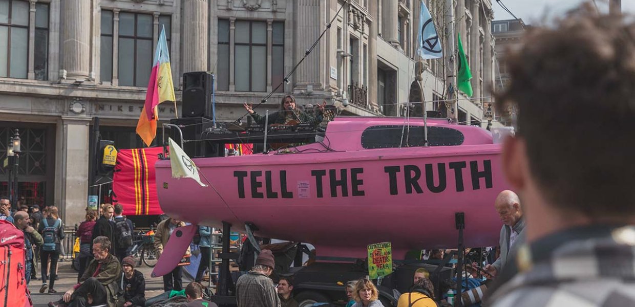 Photo of a pink blimp in a crowd of people that reads "tell the truth"
