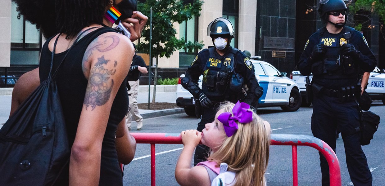 Photo of a protestor next to a small child in front of two police