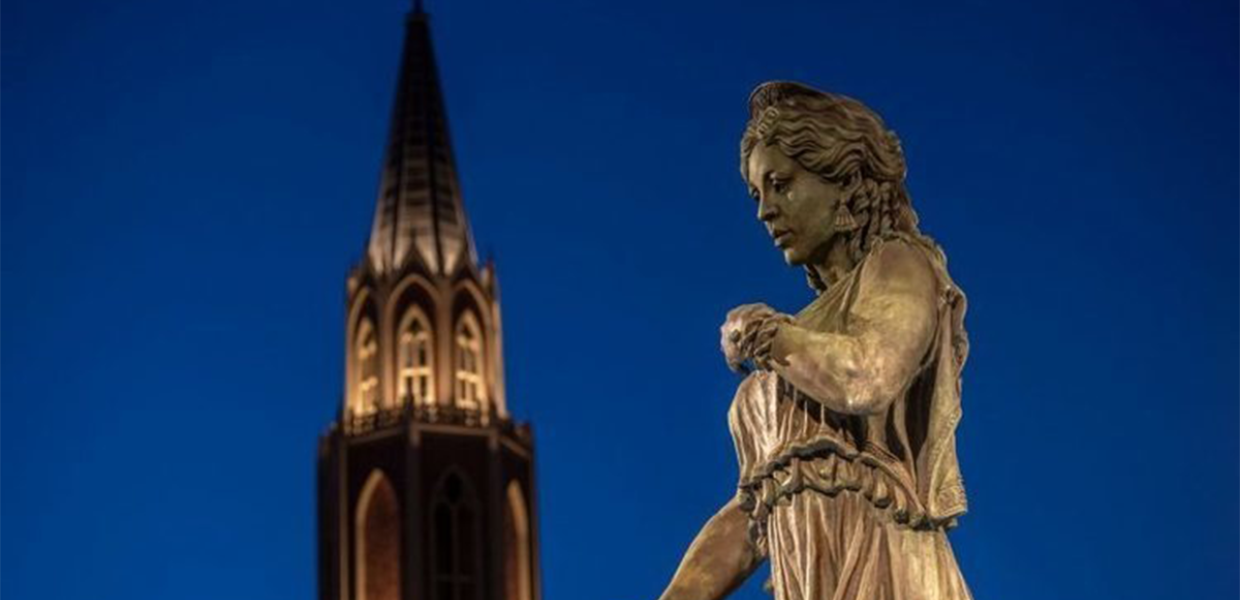 Photo o f the Hecuba statue in the USC village with the background of the McCarthy Honors College tower at dusk