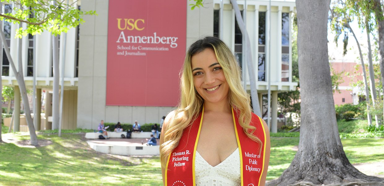 Hispanic women with red and gold graduation stole stands in front of USC Annenberg building