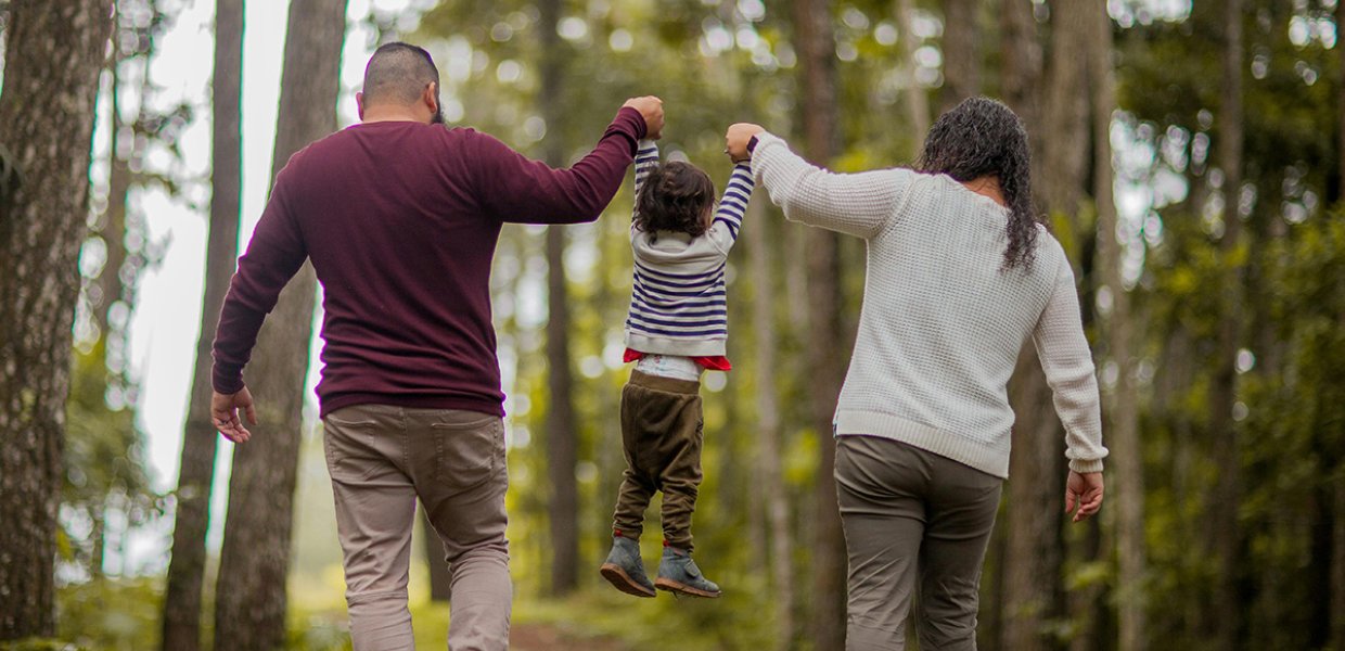 A child being held by their arms by their parents on each side of them