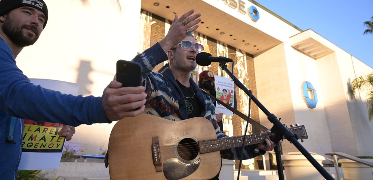 man holding phone out so man holding guitar and speaking in microphone can see