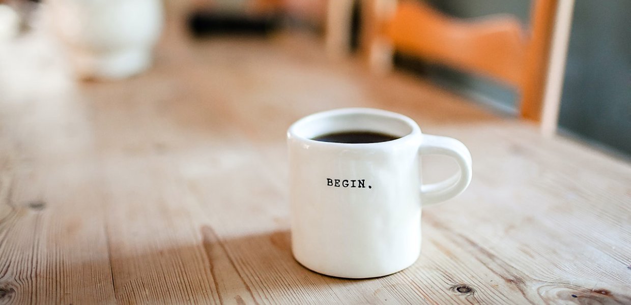 A cup of coffee on a wooden table with the word "Begin" written on it