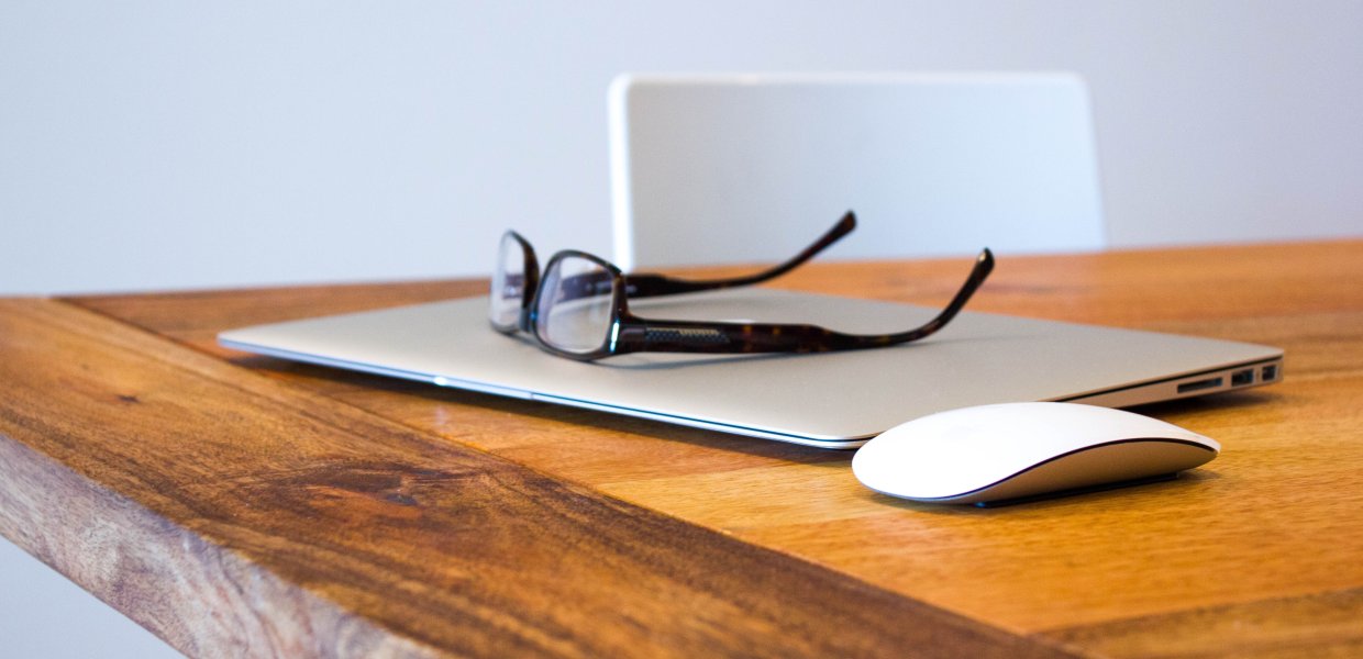 Photo of glasses on top of a laptop next to a mouse