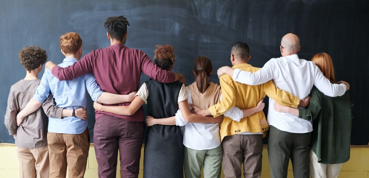 Group of people standing in doors in front of a chalk board with their arms around eachother