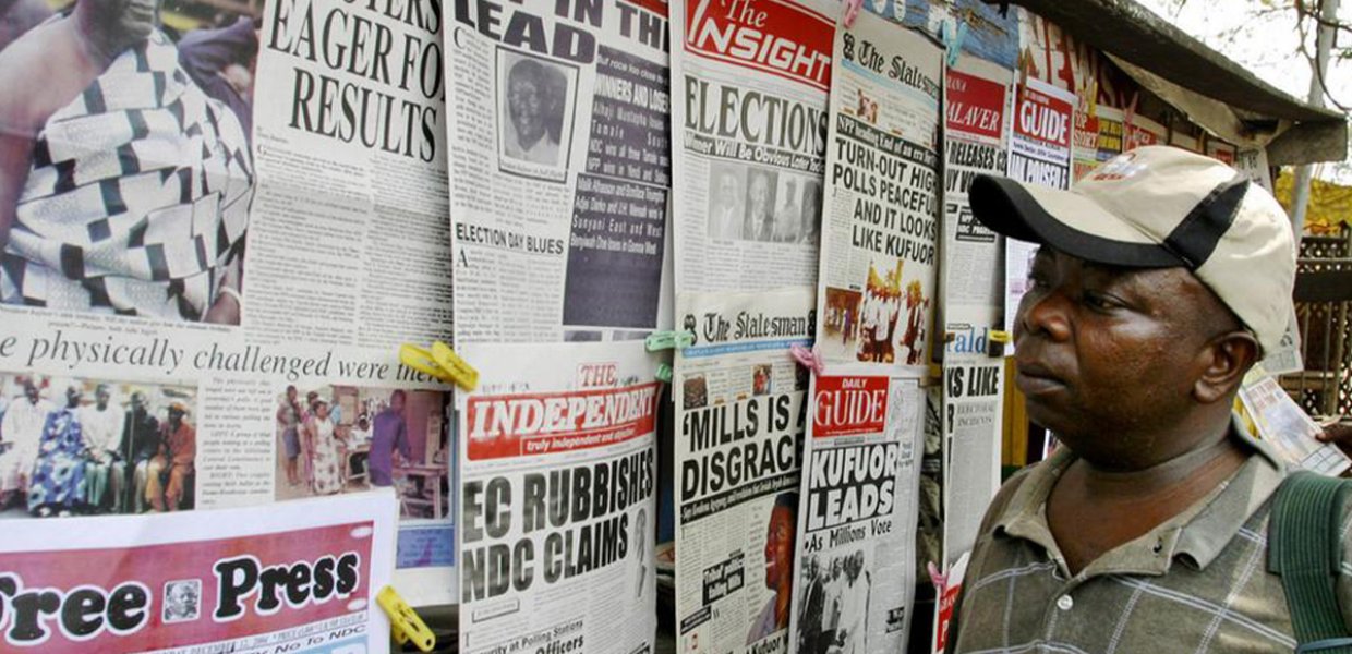 Man standing looking at a wall of newspapers