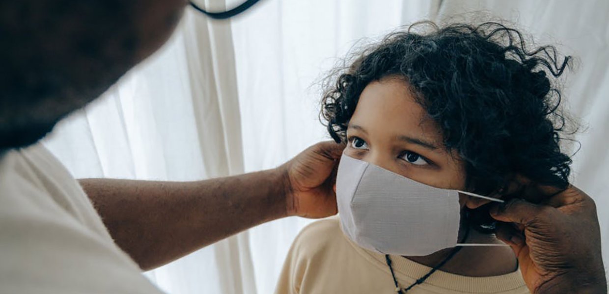 Photo of an adult putting a face mask on a child