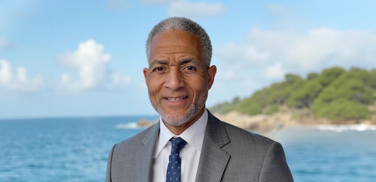 Andre Lapeyrolerie, from the shoulders up, smiling at the camera while wearing a suit and standing in front of an ocean with an island in the background. 