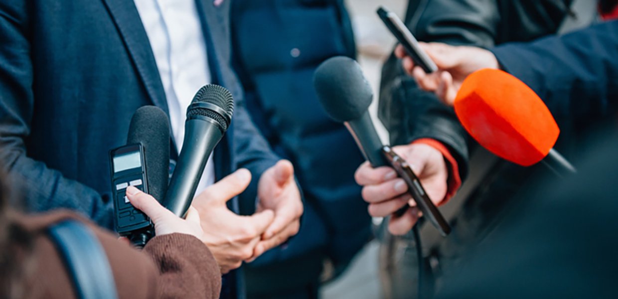 People holding up microphones, interviewing unseen politician