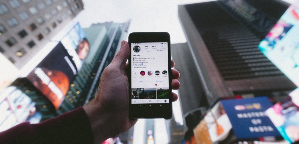Photo of a person holding a cellphone on the Instagram app with many buildings in the background