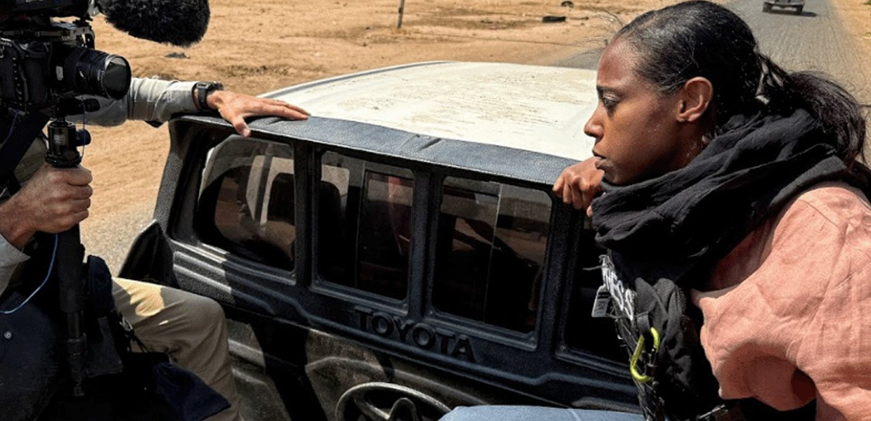 A woman looking down the barrel of a camera lens on the back of a truck