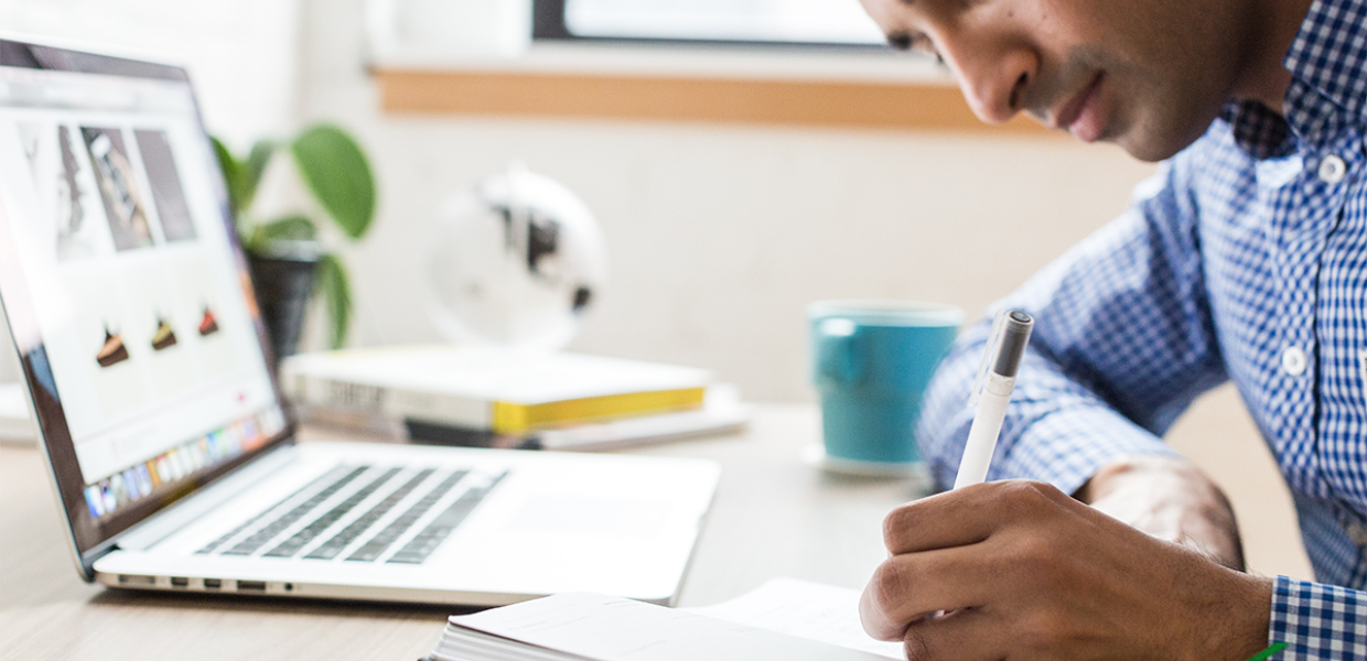 Photo of a man using a pen infront of a laptop screen