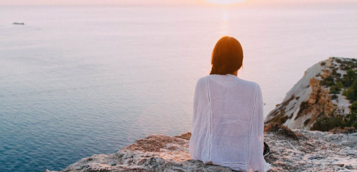 Photo of a person sitting on a mountain top facing the sea