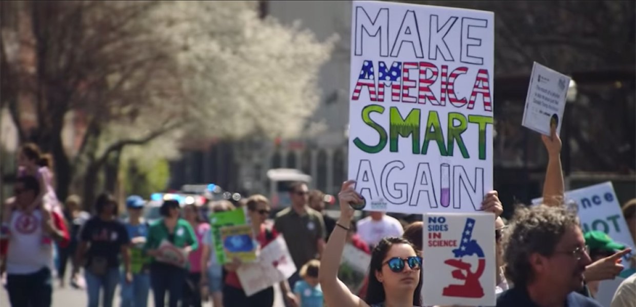 Photo of protesters with one holding a sign that says "Make America Smart Again"