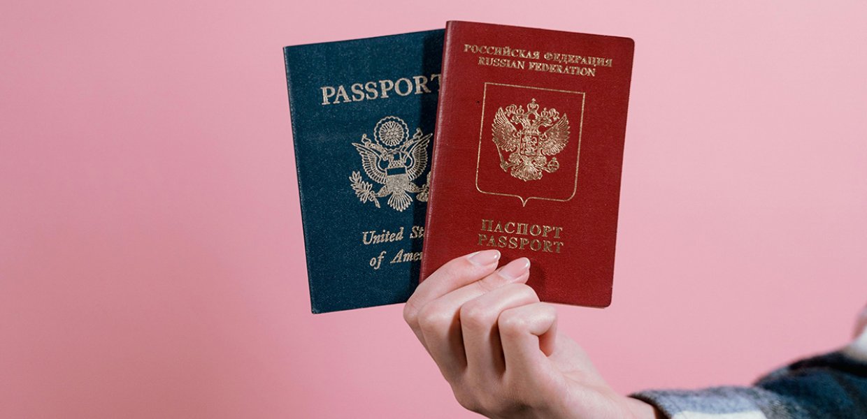 Someone holding two different passports against a pink background