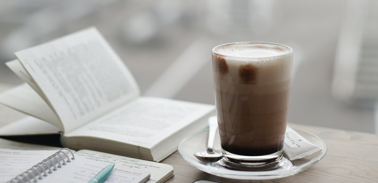 Photo of a glass of coffee with an open book next to it