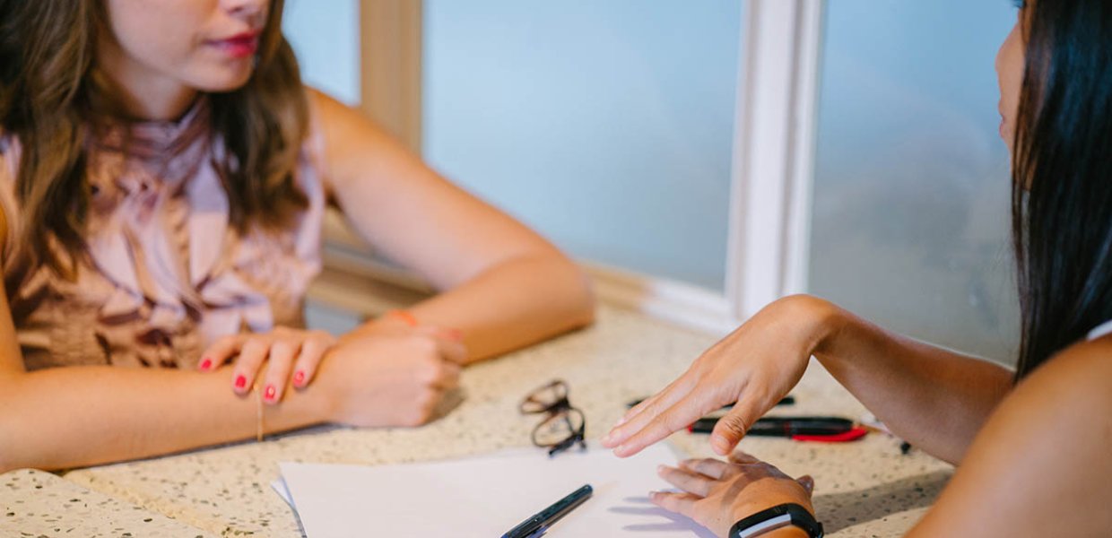 Photo of two people sitting across eachother with papers on the table, conversating