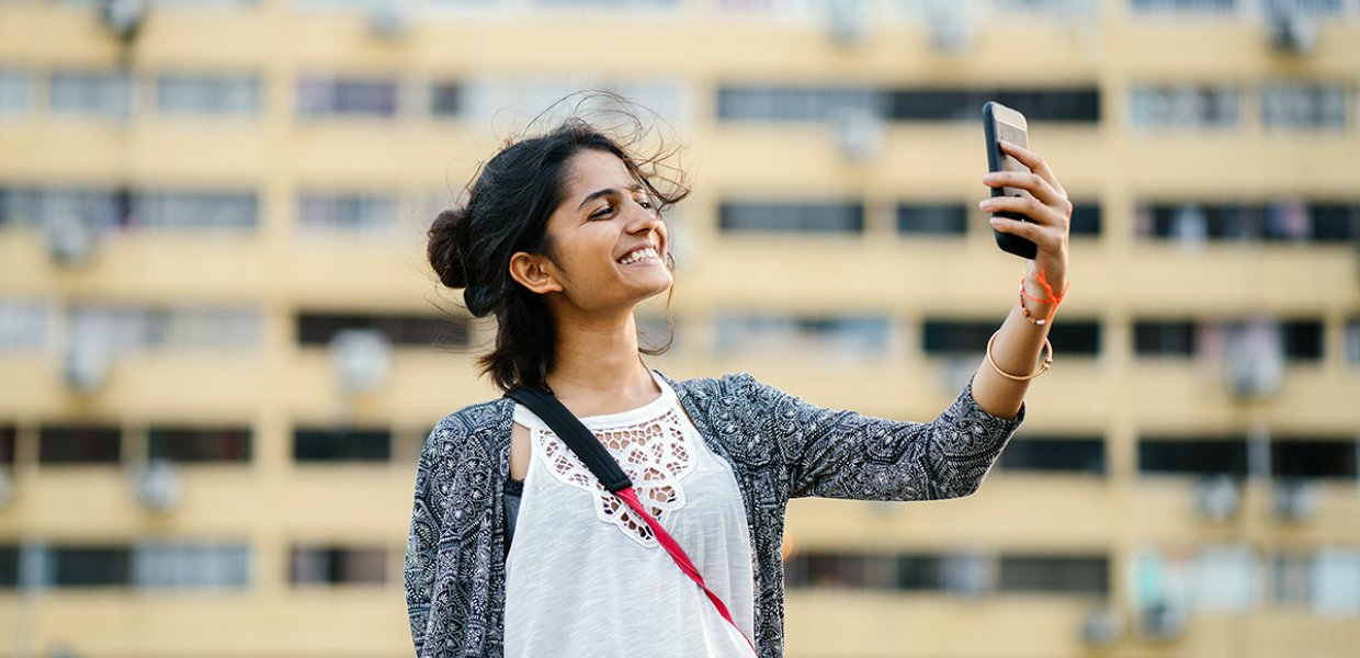 Photo of a person holding their phone and smiling at it