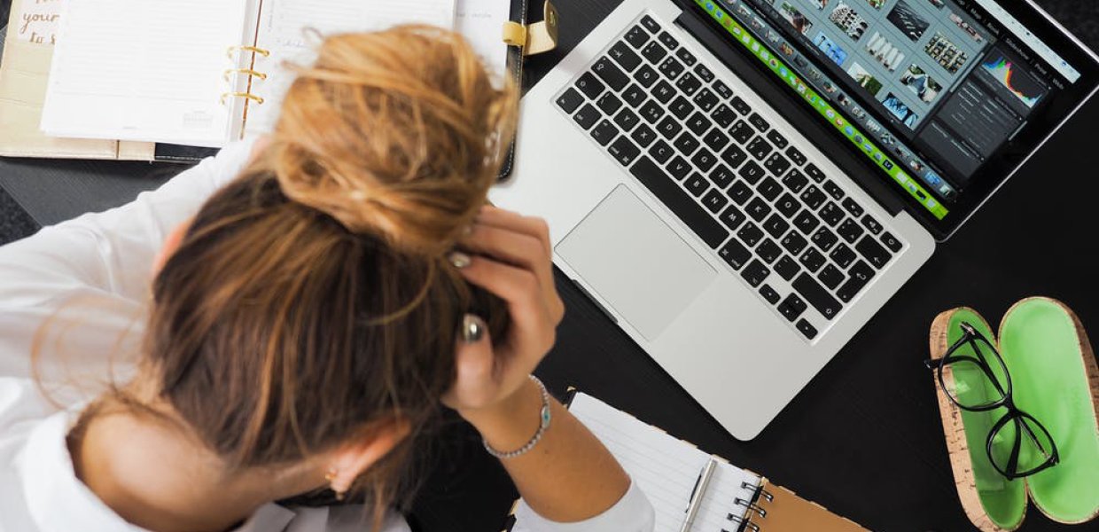 Photo of a person with their head in their hands in front of a laptop