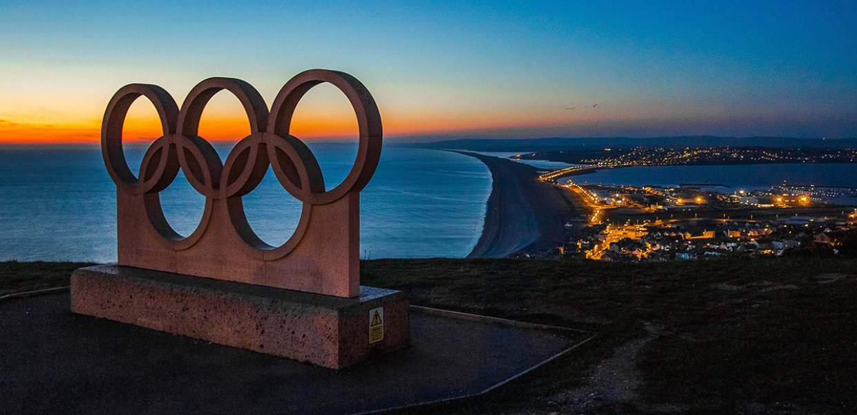 Olympic ring statue over city at sunset. 