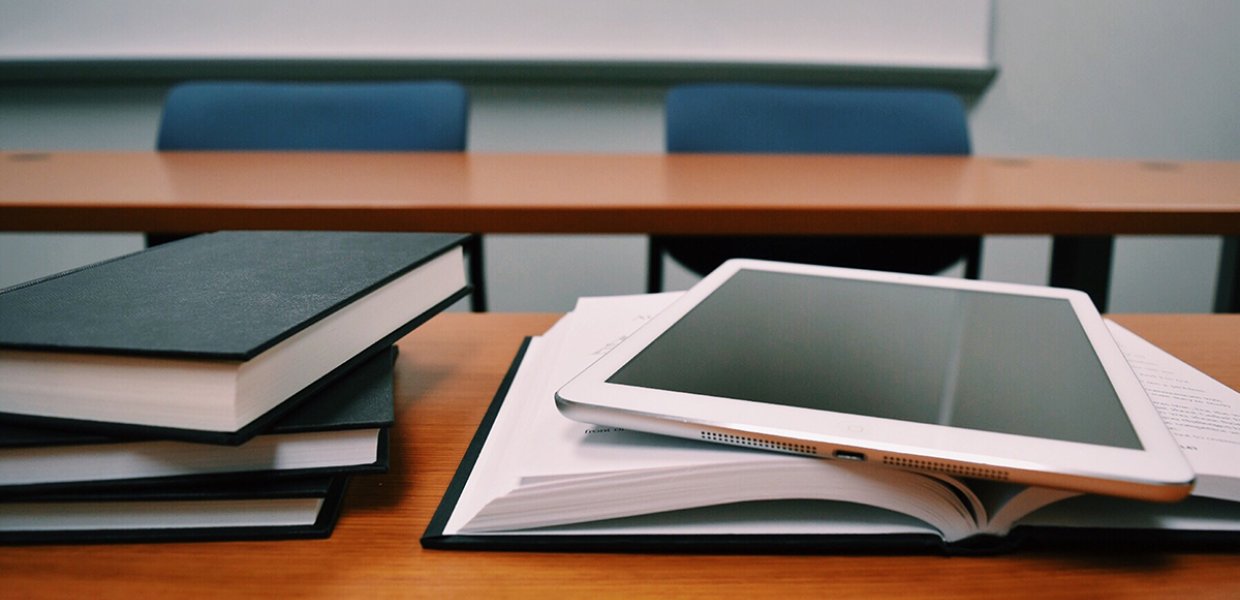 Photo of a table with a stack of books and a book with a smart tablet on it