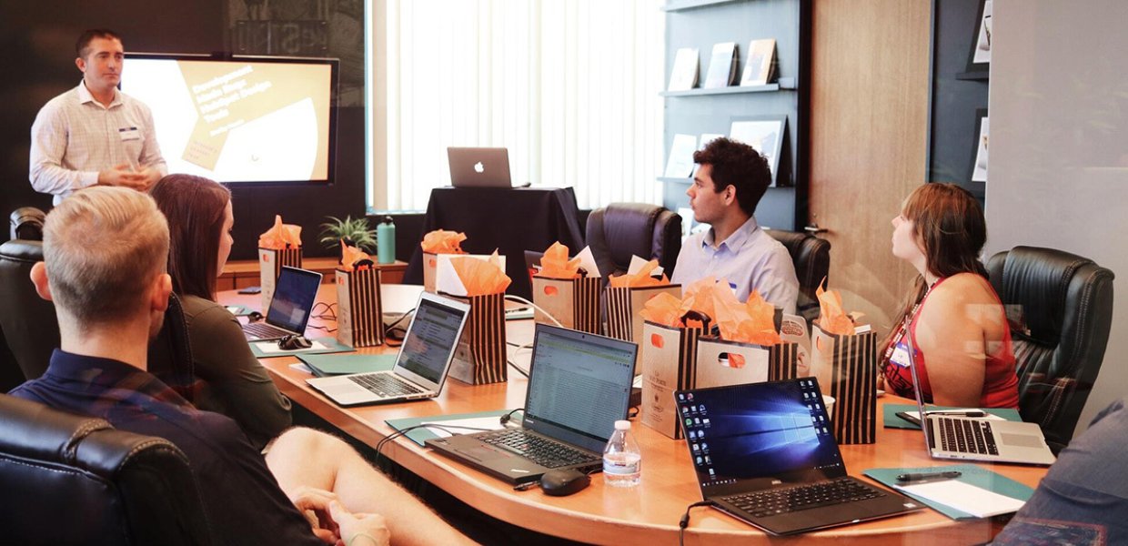 Photo of people sitting around a table with computers and bags