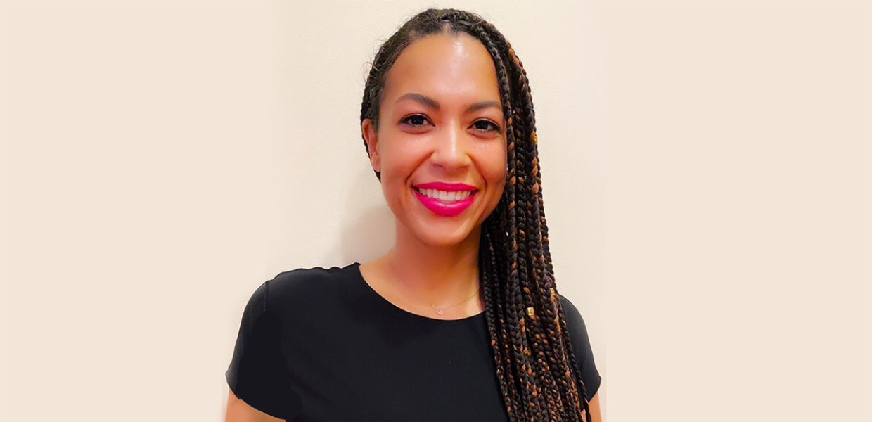 A smiling woman in front of an empty white wall.