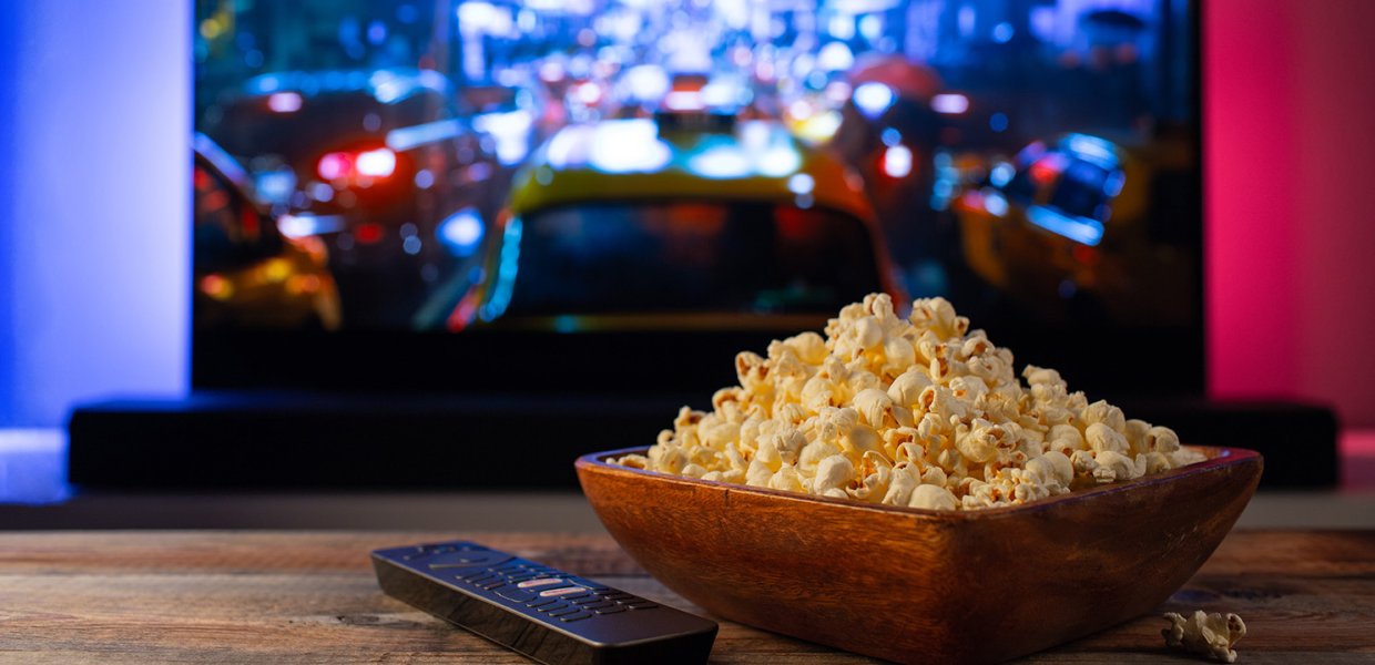 A bowl of popcorn sits on a coffee table with a remote next to it in front of a TV.