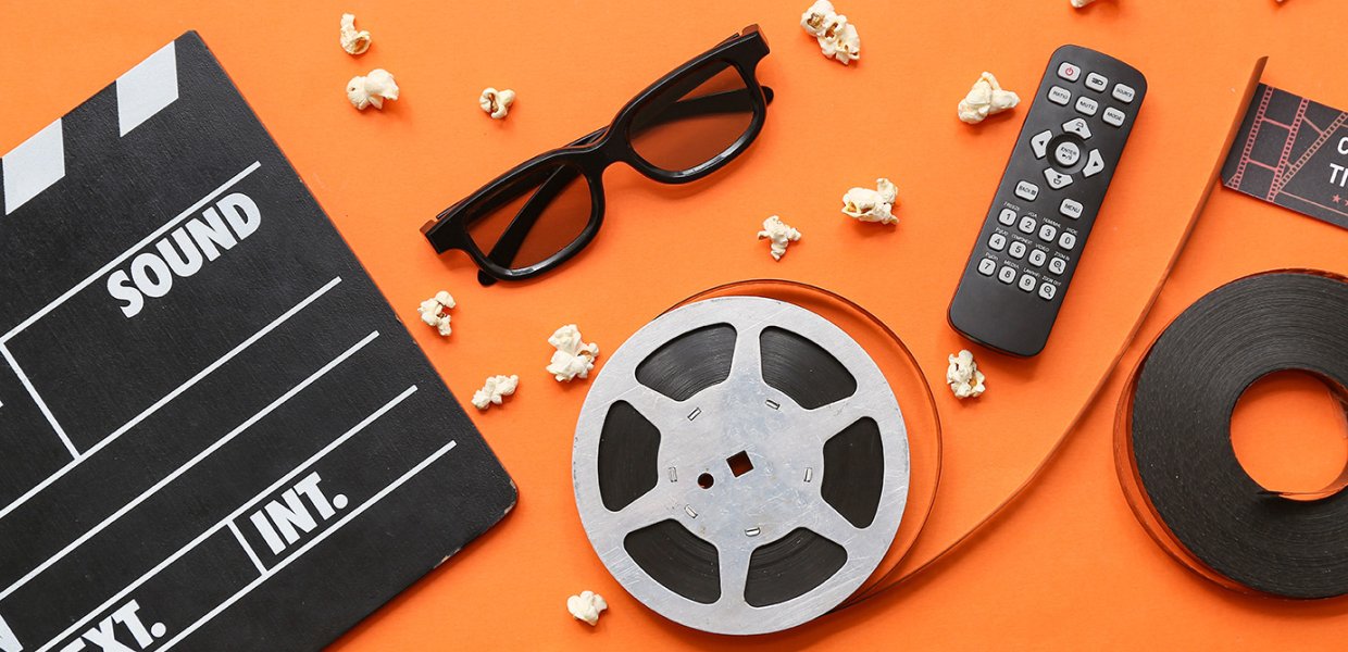 Film- and TV-related artifacts, such as a remote control, a spool of film, scattered popcorn, and a blank clapperboard, are scattered over an orange backdrop.