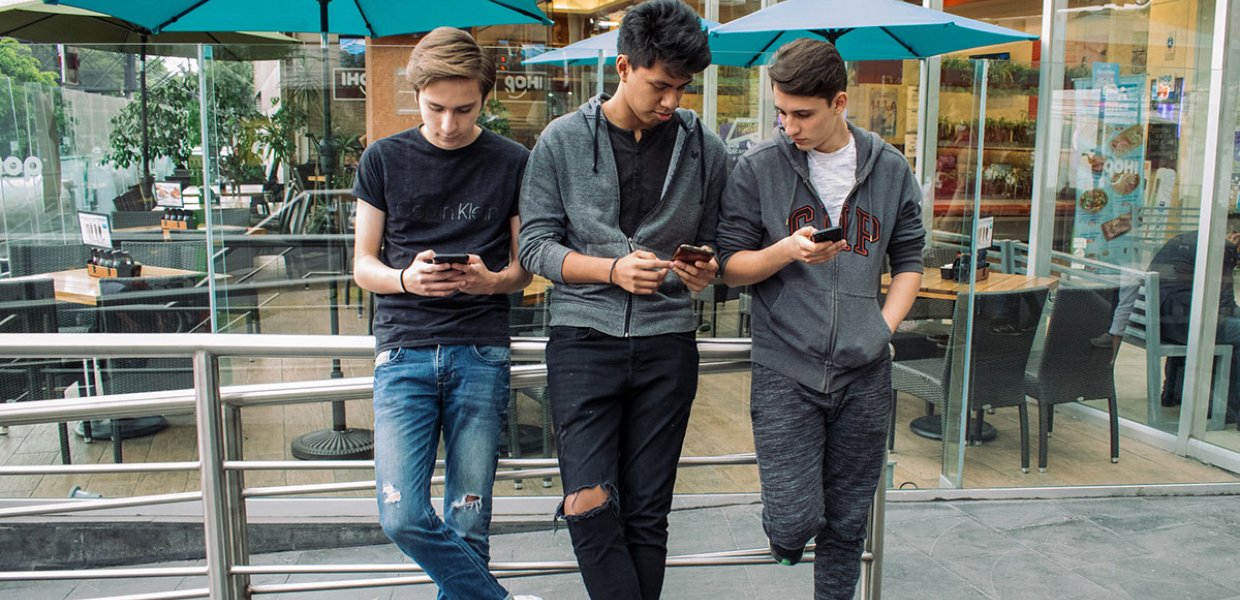 Photo of three teens standing looking at their phones