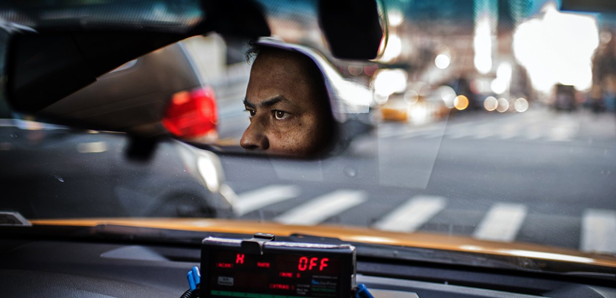 Photo of a person driving where their face is visible in the rearview mirror