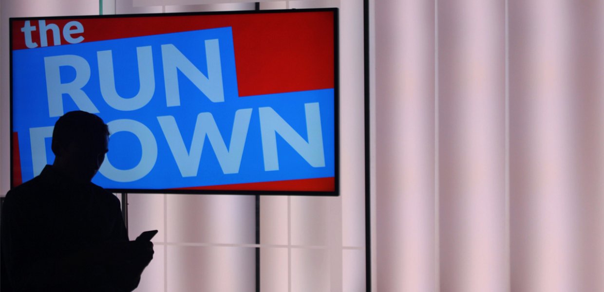 Photo of a person standing in front of a screen that says "the Run Down"