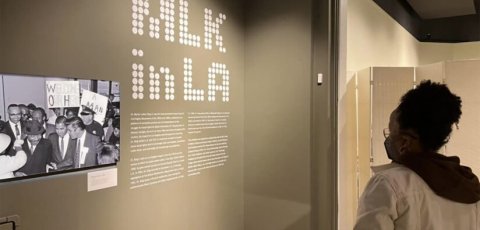 Black 20-something year old women wearing white hooded sweater looks at MLK in LA exhibit